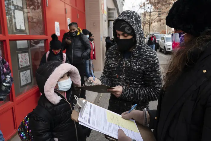 A parent, center, completes a form granting permission for random COVID-19 testing for students as he arrives with his daughter, left, at P.S. 134 Henrietta Szold Elementary School, in New York